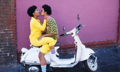 Young couple kissing on the back of a scooter.