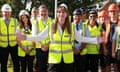 Angela Rayner in a hi-vis jacket standing with arms outstretched, smiling at the camera, as people stand in hi-vis and hard hats behind her