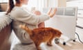 A woman and a cat warming themselves in front of an electric heater