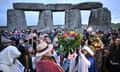 Revellers at Stonehenge, including two people holding up a floral arrangement