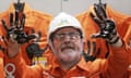 The Brazilian president, Luiz Inácio Lula da Silva, wearing orange overalls and a white hard hat, holds up his oil-covered hands to the camera.