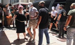 People wearing caps and masks that obscure their faces are escorted from a van as photographers take pictures of them