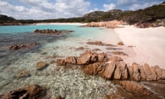 Clear water and outcrops of rock at deserted pink-tinged beach.