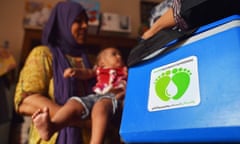 A woman holds a young child next to a blue box that reads: 'Pakistan Polio Eradication Programme'