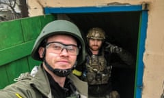 Two men in military fatigues emerge from a wartorn house