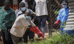 A medical attendant disinfects a man's rubber gloves outside a Hospital