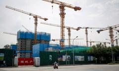 A woman rides an electric scooter next to a construction site of a housing and commercial establishment in Beijing, China