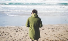 Rear view of man looking out to sea from windy beach