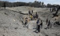 People stand in a dusty crater after an Israeli airstrike