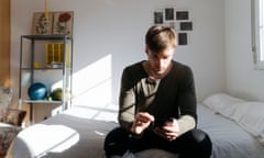 Young man sitting on bed looking at his smartphone