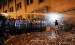 a demonstrator gestures in front of a line of riot police