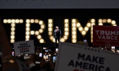 man stands in front of crowd with lights behind him reading 'trump'