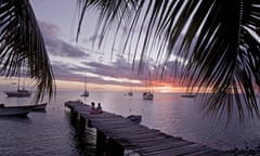 Children sitting on a wooden jetty at the sea in sunset, Dominica, Caribbean