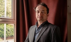 Graham Smith at home, posing by his window and a red velvet curtain.