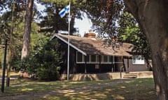 A wooden hut with tiled roof flying a Finnish flag and framned by trees