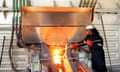 a worker in full protective gear stokes a white hot furnace at a smelting plant