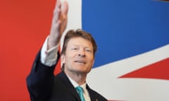 Richard Tice raises an arm while speaking in front of a union jack backdrop