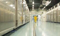 a view inside what is said to be a nuclear plant:  a man in yellow overalls walks through a brightly-lit, spotlessly clean industrial facility with large metal chambers to either side of him