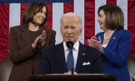 harris and pelosi look at each other and applaud behind out of focus image of biden