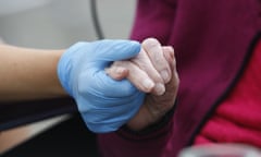 A gloved carer's hand holding an elderly person's hand.