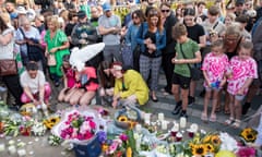 People leave flowers and candles on the ground and console each other as others look on