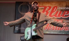 Otis Taylor performs on stage holding an aqua guitar.