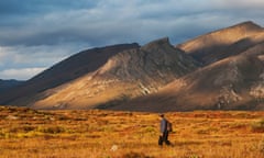 A man in a hat walking near mountain peaks
