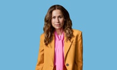 Minnie Driver wearing a mustard jacket and pink shirt against a blue background