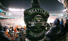 A major fan of Seattle Seahawks, the city's NFL team stands in the crowd surrounded by fellow supporters during a night game under floodlights.