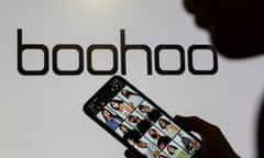 A woman poses with a smartphone showing the Boohoo app