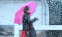 Raindrops are seen on a vehicle’s window as a woman walks by using an umbrella.