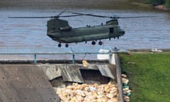 RAF Chinook helicopter prepares to drop sand bags to shore up stricken Toddbrook Reservoir.