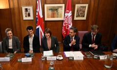 Rachel Reeves, in a slightly ruffle-topped shirt under a blazer, seated next to a woman and three men at a table in front of a Union Jack flag, a Welsh flag and three paintings on a wooden wall, leans forward a little, laughing