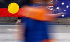 A person walks in front of the Indigenous Australian and Australian flags displayed side by side