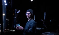 Ben Whishaw in glasses, black beanie hat and black shirt looking to camera surrounded by film studio props