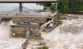 Debris fills up on a dam while brown water surges from it in the foreground