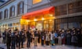 people, most of them masked, look down and clasp hands together in front of a restaurant