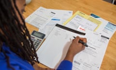 A young woman sits at her kitchen table at home checking over the household bills