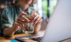 Close up of woman holding glass of water while using laptop.