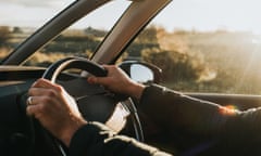 A man grips a steering wheel as dusky sunlight illuminates the car