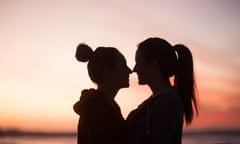 Silhouette of two lovers standing face to face<br>Outline of two young women standing very close to one another looking at each other at sunset in front of the ocean