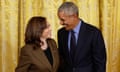 A woman in a brown blazer and a man in a suit and tie smile at each other