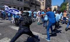 A riot police officer swings a baton at a protester