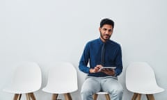 Studio shot of a young businessman using a digital tablet , sitting on a white chair with three empty chairs around him