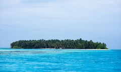 An entire forested island in the frame, with azure ocean in the foreground and on both sides, and a thick blue sky above.