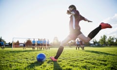 A photo of a teenage girl kicking a football towards a goal