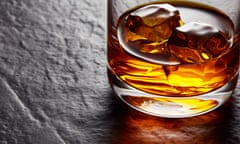 Glass of elegant whiskey with ice cubes on black stone table. 
