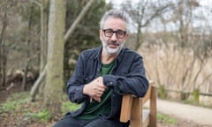 David Baddiel sitting on bench among trees.