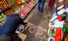 Safer shopping: a grocer chalks stop signs for his queuing customers. The UK’s chief medical officer said he expects social distancing to continue at least until the end of year.