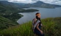 A woman wearing Indigenous dress stands on a viewpoint above a lake
